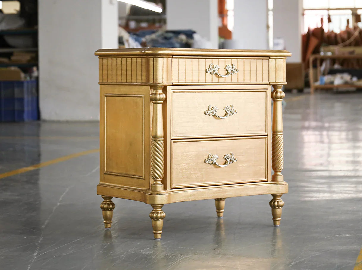 Golden three-drawer nightstand with ornate handles and wood veneer top