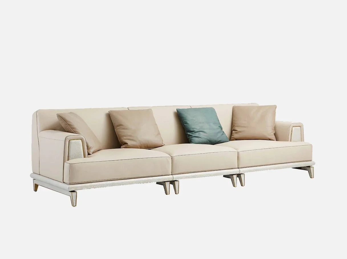 Angled view of modern sofa featuring brass-plated stainless steel frame, curved backrest, leather upholstery, and layered cushions for refined comfort.