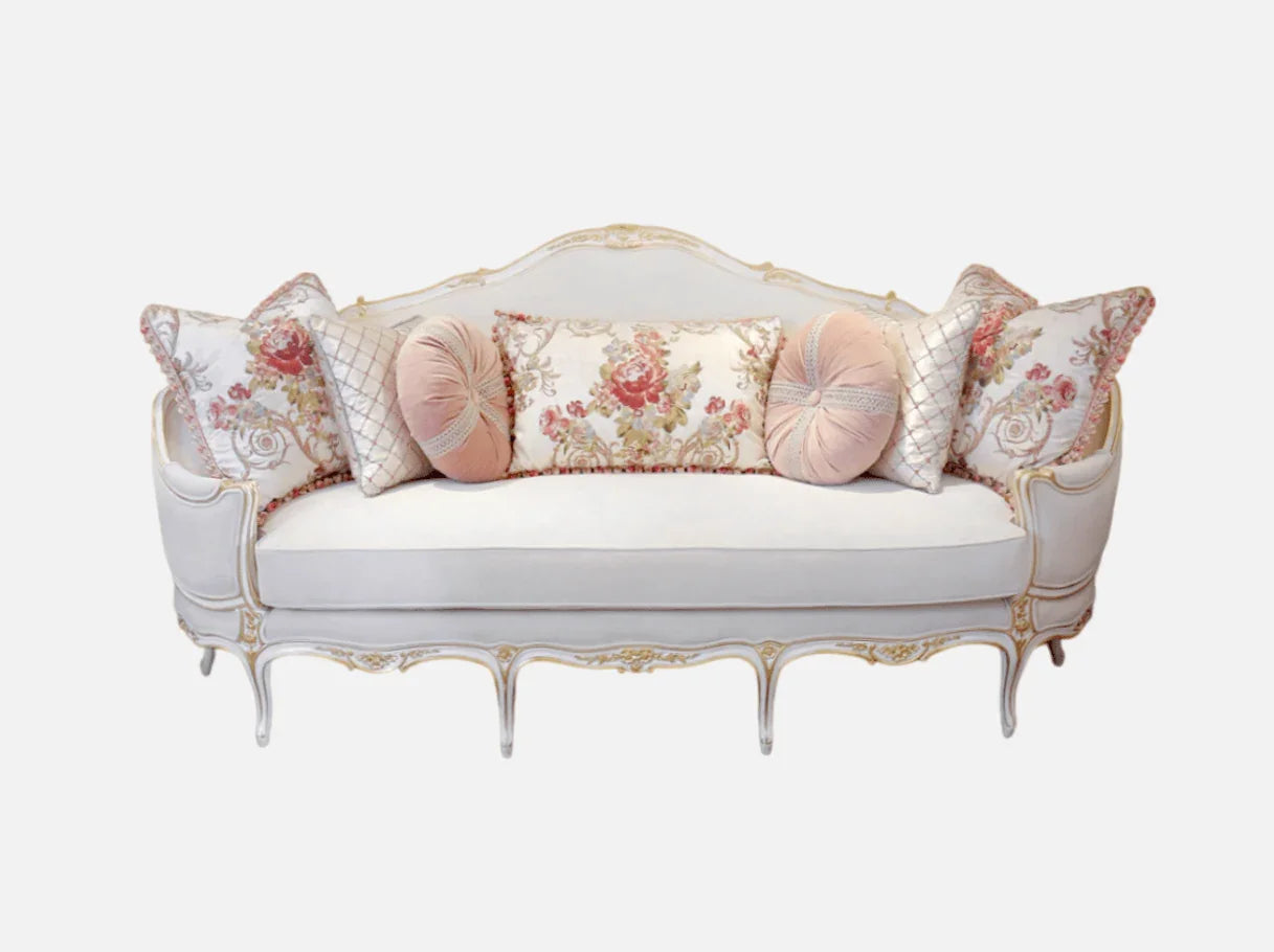Front view of a white French sofa S-1171, a classic 3-seater with pink floral pillows, hand-carved beech wood frame, and gold leaf accents.