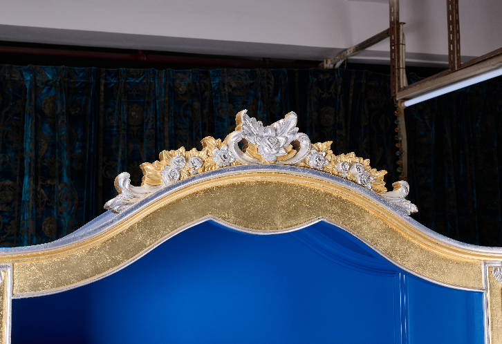 Close-up of C-056 cabinet top crest — dual gold/silver leaf carved floral motifs